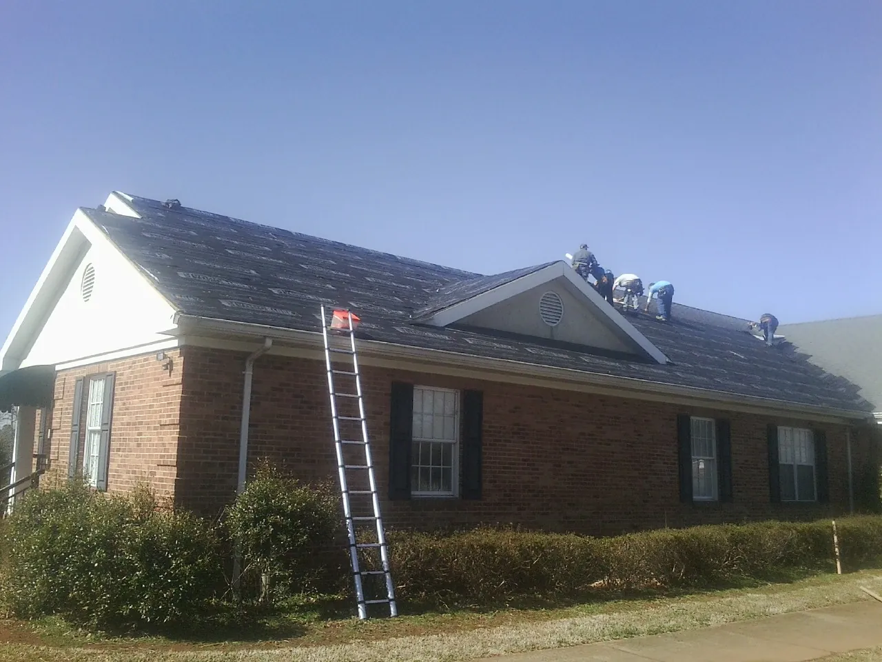 Crew tearing shingles off a brick ranch roof with a ladder set — Emergency Roof Repair work by our crew in Star