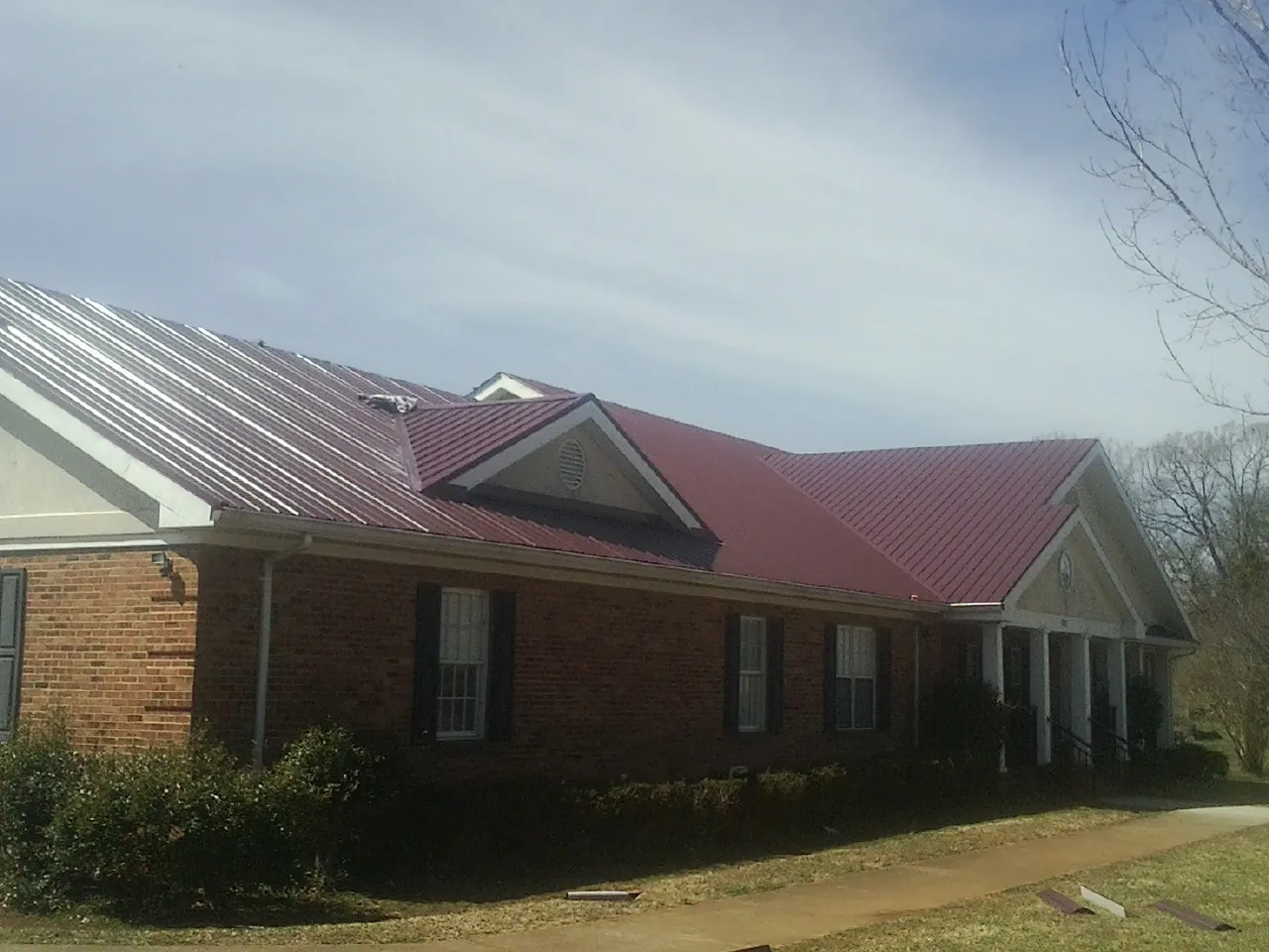 Red metal roof with gabled entries on a long brick building, from a Hail Damage Roof Repair job in Star