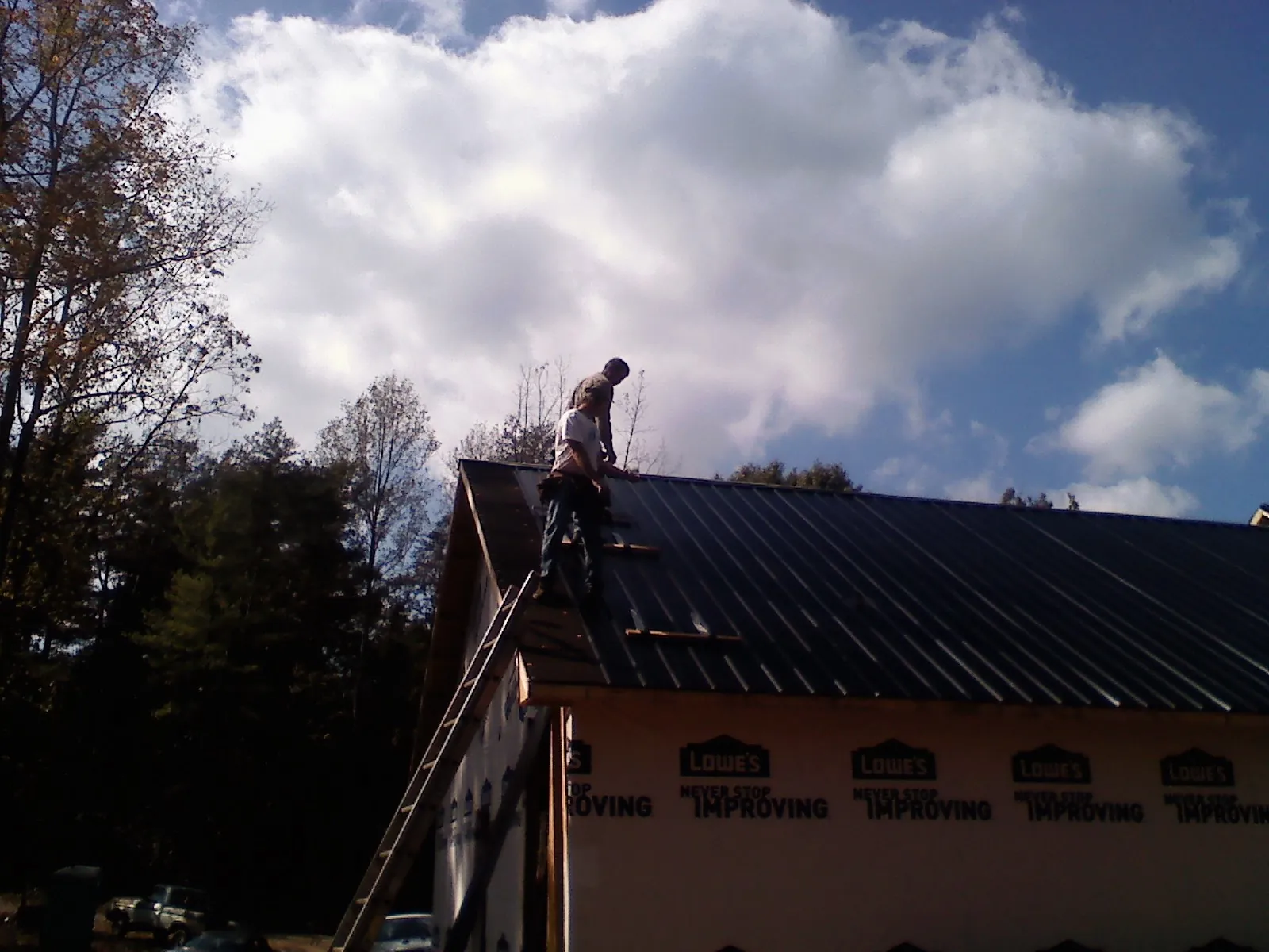 Roofer fastening dark metal panels high against a cloudy sky, from a Roof Inspection job in Star